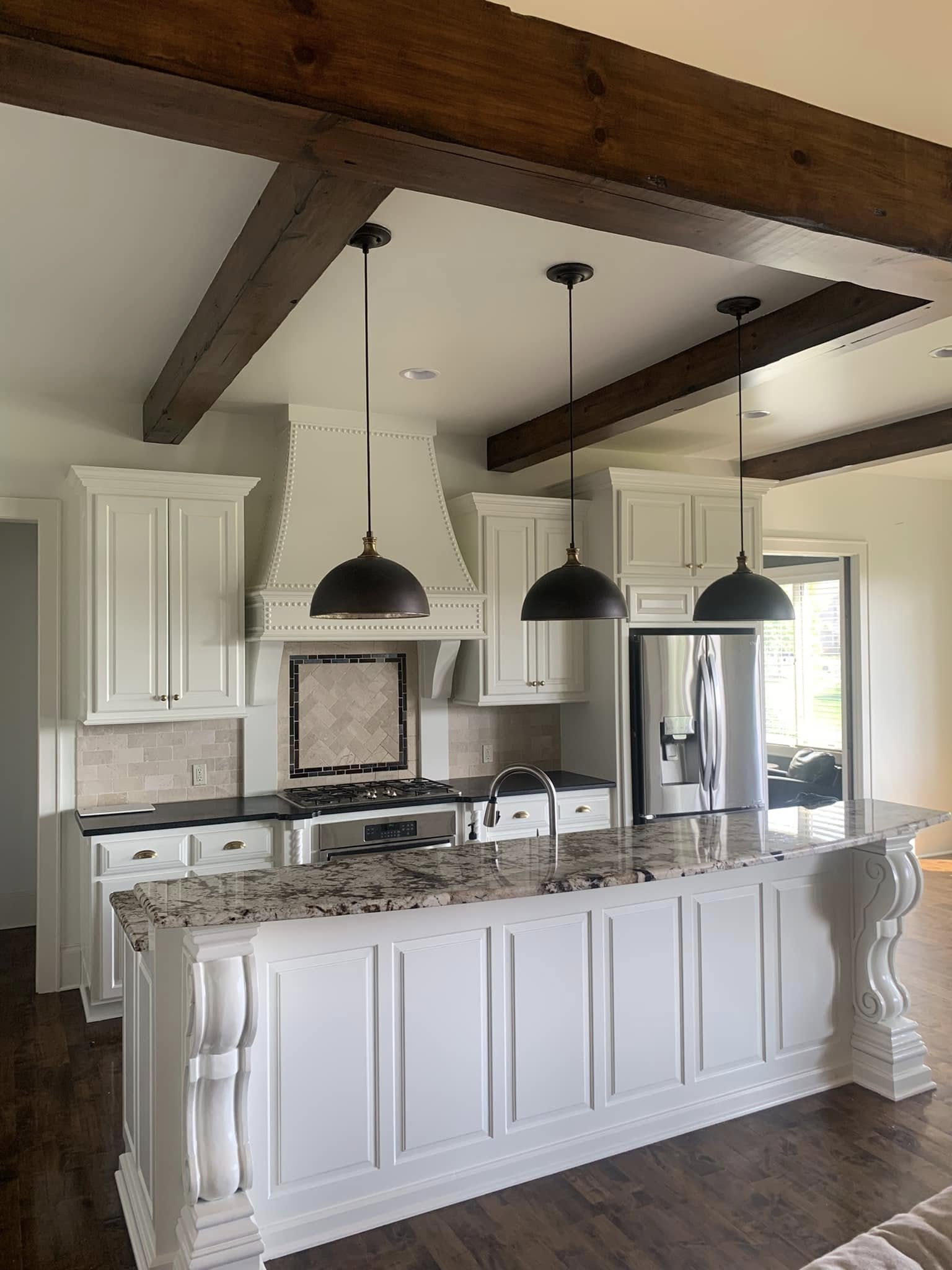 Modern farmhouse kitchen with freshly painted white cabinetry, dark wood ceiling beams, black pendant lighting, and a marbled granite island countertop.